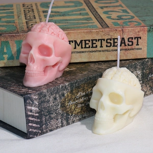 Velas aromáticas creativas de cráneo cerebral rosa y beige sobre libros para Halloween