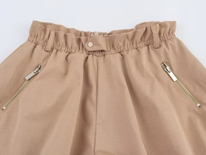 Dettaglio degli shorts a sbuffo kaki con elastico in vita, patta con bottoni e tasche zip