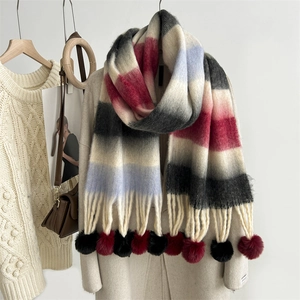Rainbow striped mohair scarf with plush pom-poms displayed on a beige coat for winter