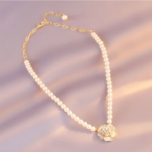 Close-up of pearl choker necklace featuring a golden floral pendant on silk fabric