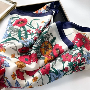 Detail of a folded square silk scarf featuring a vibrant floral pattern on a black tray