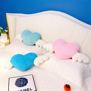 Trois coussins cœur en peluche avec ailes blanches en rose et bleu sur un lit doux