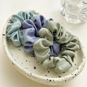 Three satin scrunchies in pastel blue, lilac, and sage green on a ceramic tray