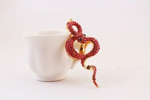Macro shot of a red crystal snake keychain draped over a white porcelain cup handle