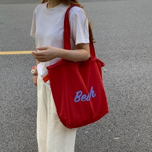 Detailed view of red canvas tote bag with blue letter print shown in a street style setting