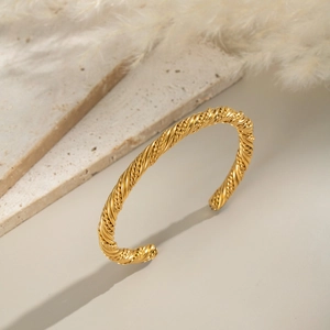 Detail of twisted rope gold open cuff bracelet on a minimalist stone display stand