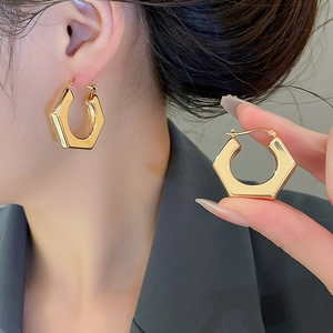 Detailed view of polished gold hexagonal earrings with a secure clasp on a female model