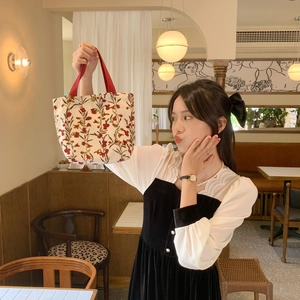 Detail of vintage corduroy tote bag with floral prints and red handles in a cafe setting