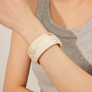 Detail of wide cream resin bangle with brown marble texture worn on model wrist