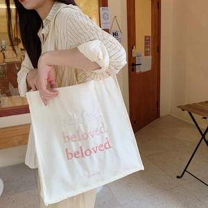 Détail du sac fourre-tout en toile crème avec broderie rose et bandoulières robustes