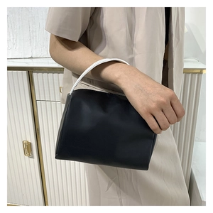 Detail of a black PU leather handbag with white round ring handle held by a model
