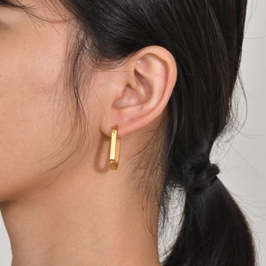 Close-up of a model wearing a polished gold octagonal hoop earring in stainless steel
