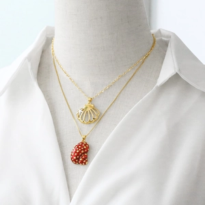Layered gold necklaces with shell and red enamel conch pendants on a white shirt