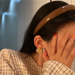 Close-up of a woman wearing a brown leather headband and golden relief earrings