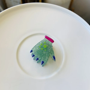 Macro view of green glitter acetate hand-shaped hair clip on a white ceramic plate