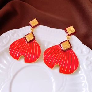Macro detail of red fishtail earrings on a vintage white plate with silk background
