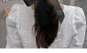 Close-up of a black mesh bow hair clip on a ponytail with a textured white top