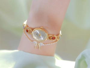 Detailed close-up of a women's gold bracelet watch with red and green gemstones