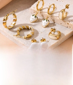 Detail of gold titanium steel strawberry pendant earrings and white enamel hoops