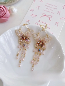Détail de boucles d'oreilles papillon dorées avec cristaux roses et perles sur plateau