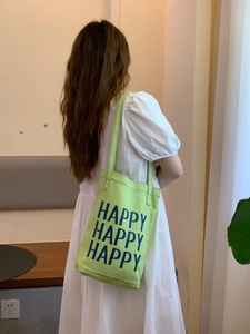 Detail of light green canvas tote bag with blue Happy text print on a female model