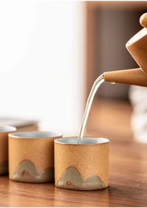 Detail of a brown ceramic teapot pouring tea into Japanese style cups with mountain design