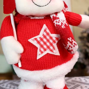 Close-up of a Christmas doll wearing a red knit sweater with a star patch and soft fur trim