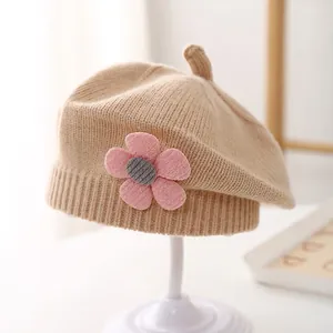 Close-up of a light camel knitted baby beret with a 3D pink flower and grey center