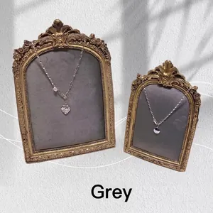 Vintage gold frame display with heart and circle pearl necklaces on a grey texture background
