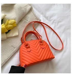 Detail of orange quilted crossbody bag featuring V-shaped texture on a soft white fabric