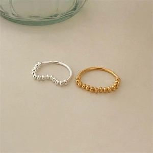 Minimalist 925 sterling silver beaded rings in gold and silver finish shown on a warm surface