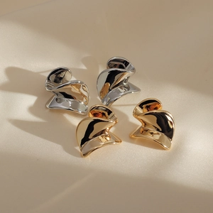 Macro shot of abstract twisted metal stud earrings in gold and silver on beige silk