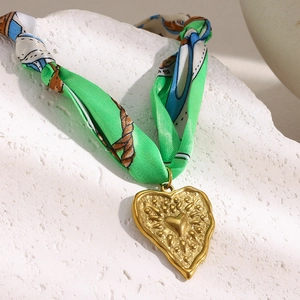 Detailed close-up of a green silk ribbon necklace with a textured gold heart pendant