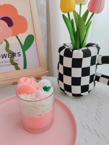 Close-up of pink rose-shaped soy wax candle with cream frosting in a glass cup
