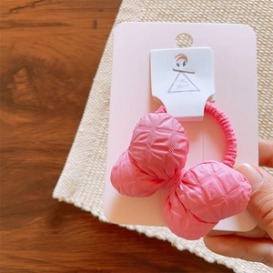 Detail of pink cotton-filled fabric bow hair tie on display card with embossed texture