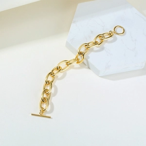 Detailed macro view of a gold chunky chain bracelet featuring an OT toggle clasp on marble