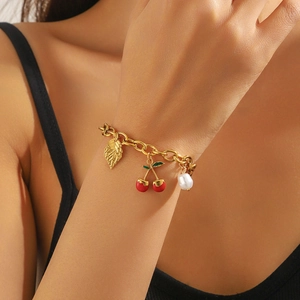 Detail of gold chain bracelet with cherry charms, green leaf and pearl on wrist
