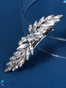 Detail of silver feather hair clip featuring sparkling rhinestones on blue background