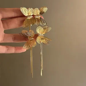 Close-up of golden butterfly earrings with sparkling crystals and long chain tassels