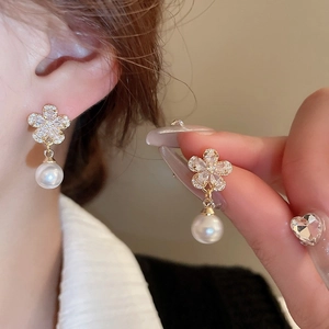 Macro detail of gold plated five-petal flower earrings with zircon and drop pearl