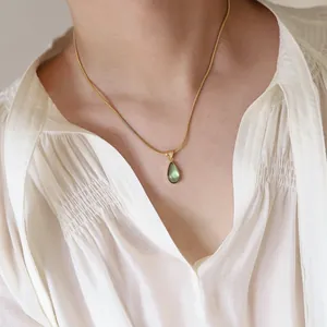 Detailed view of water drop green pendant on golden snake chain worn by a model