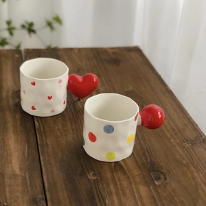Detail of hand-pinched ceramic mugs with red heart and colorful dots patterns on a wood table
