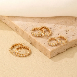 Golden hoop earrings with round pavé zircon stones on a beige stone surface