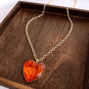 Detailed view of amber heart pendant with gold chain resting on a rustic wooden tray