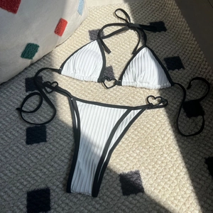 White ribbed bikini set with black trim and heart-shaped metal buckles on flat lay rug
