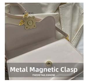 Detail of the vintage gold clover-shaped magnetic clasp on a beige leather saddle bag