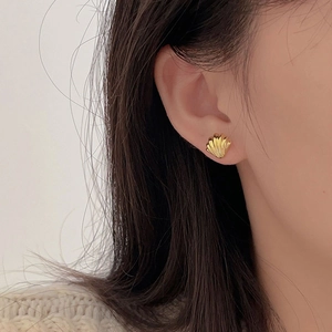 Macro shot of minimalist shell-shaped golden stud earrings with fine line texture on ear