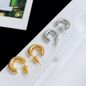 Macro shot of thick gold and silver C-shaped hoop earrings set on a white display tray