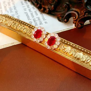 Vintage gold oval earrings with ruby-red stones and zircon halo on retro background