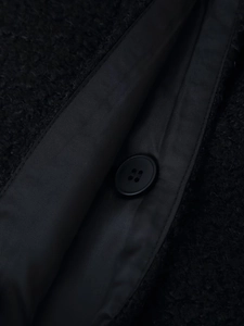 Close-up of black fuzzy wool coat featuring a four-hole round button and textured fabric